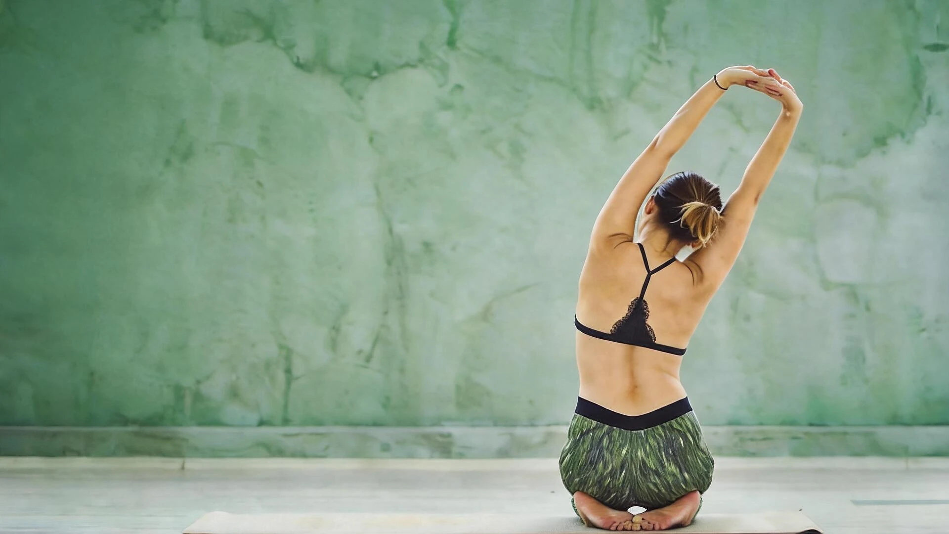 Mujer practicando yoga, estirándose de espaldas frente a un muro verde en Centro Kanda, estudio de yoga en Lomas de Bezares, CDMX